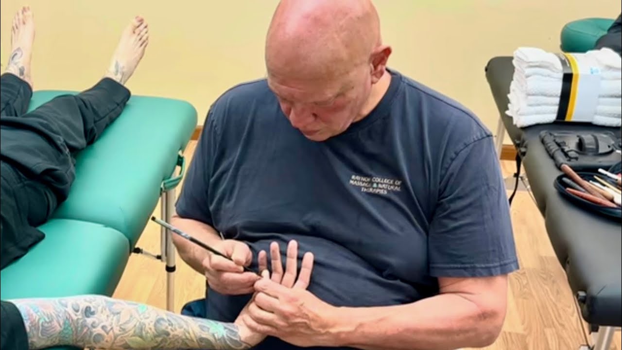 Brandon diagnosing tension in Curtis and massaging his fingers with chopsticks to help his shoulder